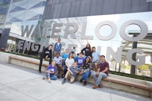 A group of students sitting in front of the Waterloo Engineering sign on the E7 building