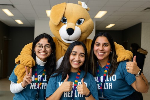 three female students standing with a bear mascot, smiling