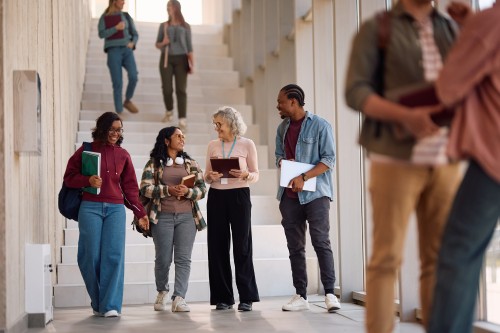 three students walking with a retiree in a hall by some stairs