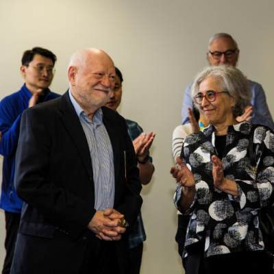 A group of people, including an older man and woman, engaged in conversation at a formal event, with others in the background.