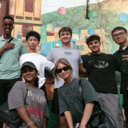 A group of students smiling in front of a painted mural