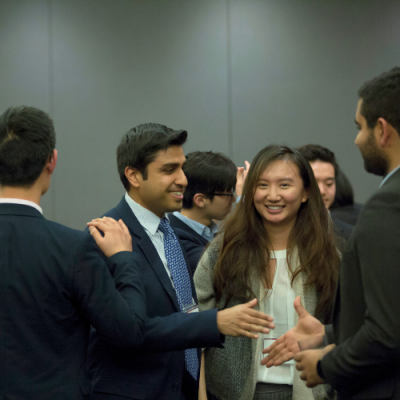 Young professionals in business attire engaged in conversation, with a woman smiling while shaking hands with a man.