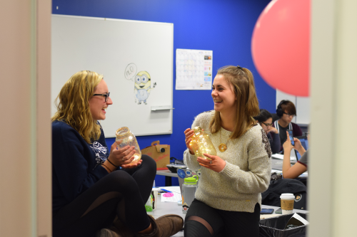 Two students holding glowing jars with lights in them and laughing in a classroom