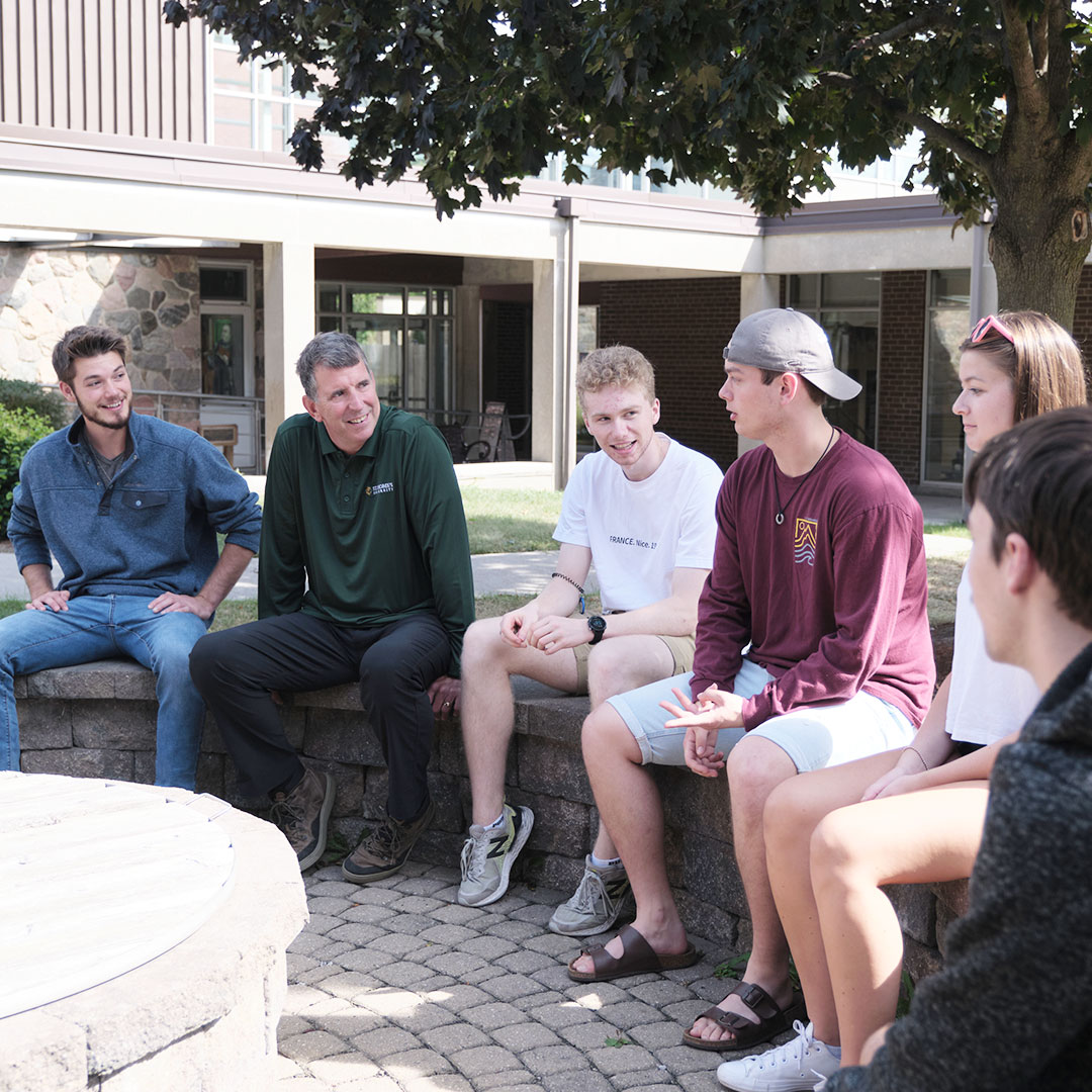 a group of five students and an advisor talking in the courtyard