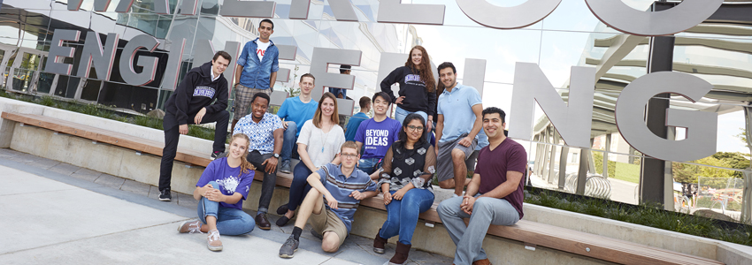 a group of engineering graduates sits in front of an engineering building on campus