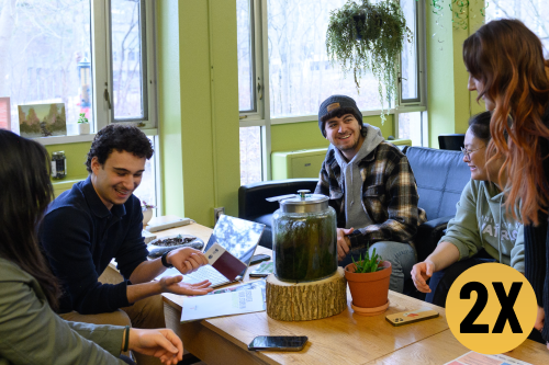 three students sitting around a table, a text circle with '2X' on top