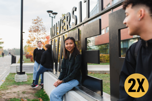 Four students standing and sitting on the main University of Waterloo sign on campus