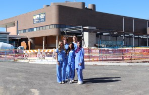 Five students in scrubs standing in front of the construction for the new Waterloo Eye Institute