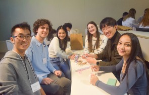 Six students sitting around a table smiling.