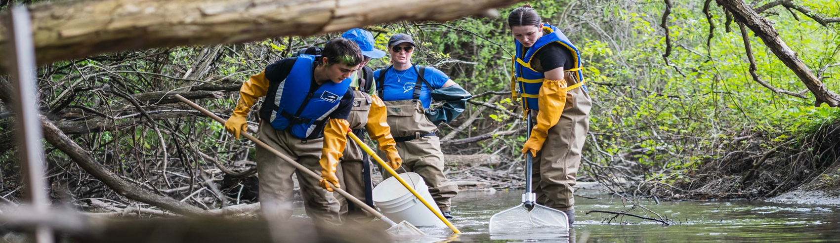 two students cleaning out a river bed with advisors watching in the back
